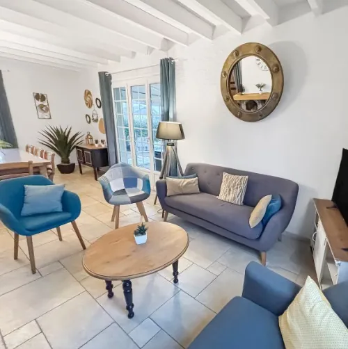 Salon lumineux avec canapés bleus, table basse en bois et miroir hublot