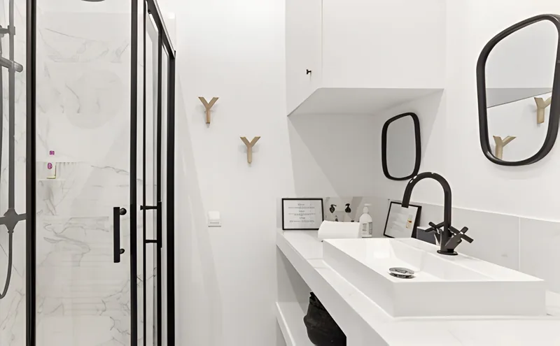 Salle d'eau blanche avec douche vitrée et robinetterie noire
