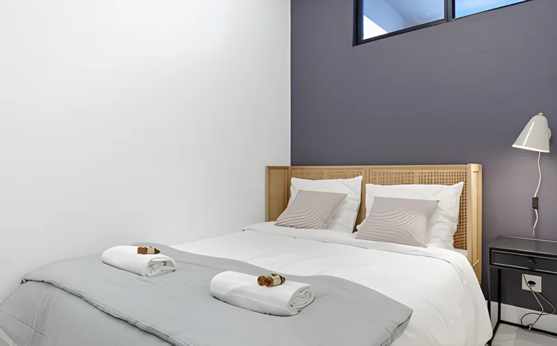 Chambre au mur gris ardoise, tête de lit en cannage et serviettes pliées sur le lit